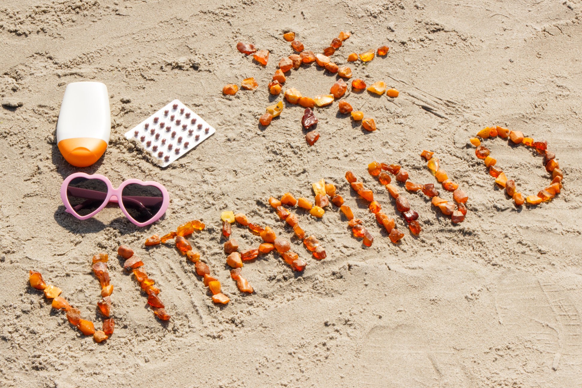 Medical pills, inscription vitamin D and accessories for sunbathing on sand at beach, concept of prevention of vitamin D deficiency